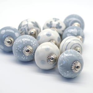 Puede incluir: Una colección de diez pomos de armario de cerámica en varios tonos de azul y blanco con un acabado plateado. Los pomos presentan diferentes patrones, incluyendo lunares, diseños florales y rayas.