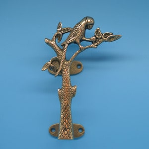 Könnte beinhalten: Dekorativer Türgriff aus Metall mit einem Papagei auf einem Ast. Der Griff ist bronzefarben und hat ein detailliertes Design. Der Griff ist auf einem blauen Hintergrund montiert.