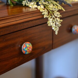 以下が含まれることがあります： 花柄のセラミックノブが付いた木製の引き出しが2つ。引き出しは濃い木製のテーブルの上にあります。