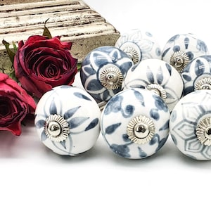 Op de afbeelding: Een verzameling van tien witte keramische kastknoppen met blauwe bloemenpatronen. De knoppen hebben een zilveren afwerking en zijn in een cluster gerangschikt.