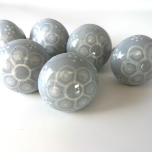 May include: Six grey ceramic decorative spheres with white floral patterns. The spheres are arranged on a white surface, showcasing their glossy finish and intricate designs. These decorative spheres are ideal for home decor.