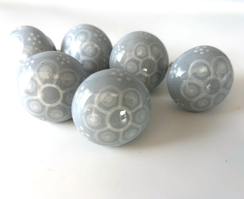 May include: Six grey ceramic decorative spheres with white floral patterns. The spheres are arranged on a white surface, showcasing their glossy finish and intricate designs. These decorative spheres are ideal for home decor.