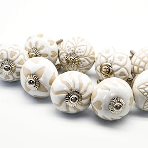 May include: Set of ten white ceramic cabinet knobs with a beige floral design. Each knob has a gold-colored metal base.