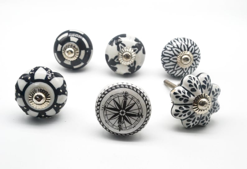 K&ouml;nnte beinhalten: Sechs schwarze und wei&szlig;e Keramik-Schrankkn&ouml;pfe mit verschiedenen Mustern. Die Kn&ouml;pfe haben eine goldfarbene Metallbasis.