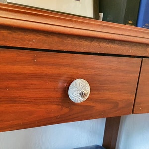 Op de afbeelding: Een houten consoletafel met twee laden. De laden hebben decoratieve witte keramische knoppen. De tafel is donker roodbruin.