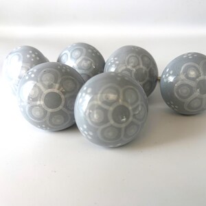 May include: Seven grey ceramic spheres with a glossy finish. Each sphere has a white floral pattern. The spheres are arranged on a white surface, creating a decorative display.