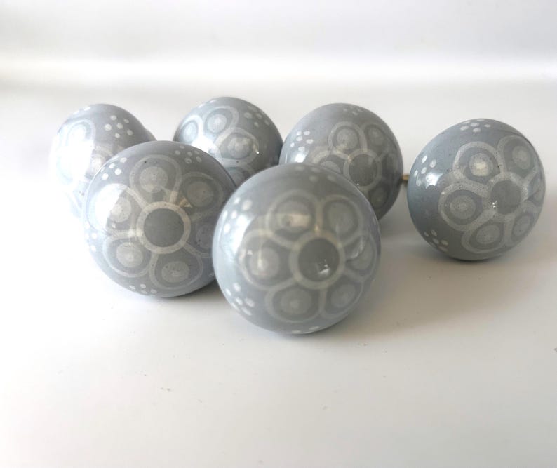 May include: Seven grey ceramic spheres with a glossy finish. Each sphere has a white floral pattern. The spheres are arranged on a white surface, creating a decorative display.
