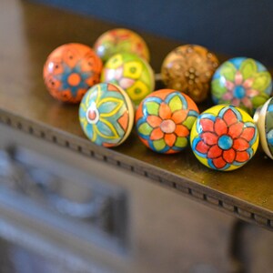 以下が含まれることがあります： 花柄のカラフルなセラミックノブのセット。ノブは青、緑、赤、黄、オレンジの色合いで塗られています。