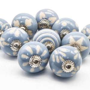 May include: A set of ten blue ceramic cabinet knobs with white floral designs. Each knob has a silver metal base.