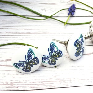 May include: Four white ceramic cabinet knobs with a butterfly design in shades of blue, green, and yellow. The knobs have silver metal stems.