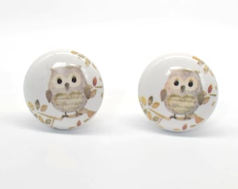 May include: Two white ceramic cabinet knobs with a painted owl design. Each knob features a brown owl perched on a branch with autumn-colored leaves. The knobs are round and have a glossy finish.