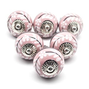 May include: Six pink ceramic cabinet knobs with a white floral pattern and silver accents.