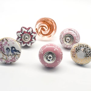 Puede incluir: Seis pomos de armario de cerámica con varios diseños florales y de pájaros. Los pomos son en tonos de rosa, blanco y dorado.