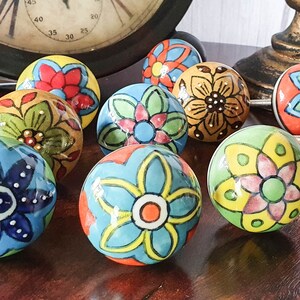 以下が含まれることがあります： 花柄のカラフルなセラミック製のドアノブが10個。各ノブは、青、緑、黄、オレンジ、赤、ピンクの色合いで、異なる花柄が描かれています。