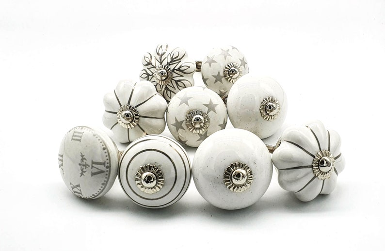 以下が含まれることがあります： 星、ストライプ、時計の文字盤など、さまざまなデザインが施された白いセラミック製のキャビネットノブ10個のセット。ノブはシルバー仕上げで、どんな部屋にもエレガントな雰囲気を添えるのに最適です。