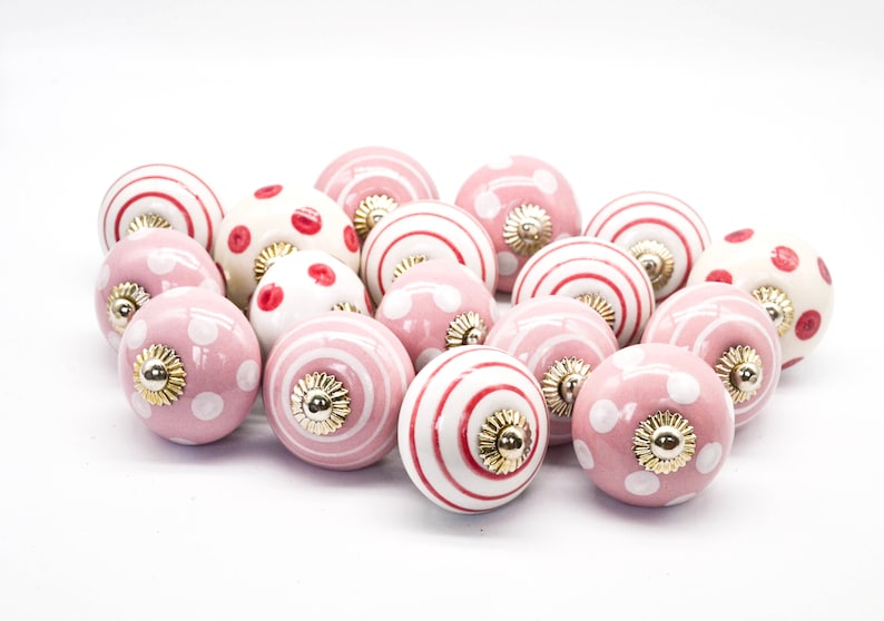 May include: A collection of pink and white ceramic drawer knobs with red polka dots and stripes. The knobs have a gold-colored metal base.