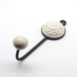 May include: A white ceramic hook with a geometric design on the top, attached to a black metal hook.