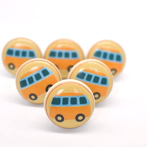 May include: Six round cabinet knobs featuring a light yellow background and a cartoon orange bus design with blue windows. The knobs have a white stripe around the middle and black wheels. The knobs are arranged in a semi-circle.