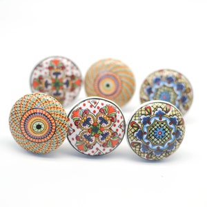 May include: Six decorative ceramic cabinet knobs with colourful, intricate patterns. The knobs feature a variety of designs, including floral and geometric motifs, in shades of red, blue, orange, and green. Each knob is approximately 3.8 cm in diameter.