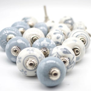 May include: A collection of 18 ceramic drawer knobs in a light blue and white colour scheme. The knobs feature a variety of floral and geometric patterns.