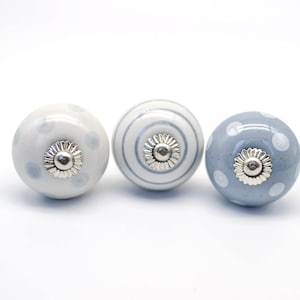 May include: Three ceramic cabinet knobs with a white background and blue polka dots, stripes, and solid blue designs. Each knob has a silver metal centre.