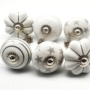 以下が含まれることがあります： グレーのアクセントが付いた白いセラミック製のキャビネットノブ6個セット。ノブは、ストライプ、星、波状の縁など、さまざまなデザインが施されています。