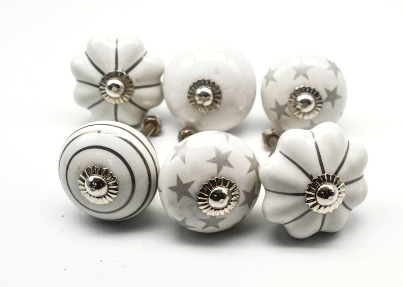 以下が含まれることがあります： グレーのアクセントが付いた白いセラミック製のキャビネットノブ6個セット。ノブは、ストライプ、星、波状の縁など、さまざまなデザインが施されています。