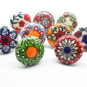 Puede incluir: Surtido de diez pomos de cajón de cerámica coloridos con diseños florales y geométricos. Los pomos son redondos y tienen un fondo blanco con varios colores, incluidos el rojo, el azul, el verde, el naranja y el negro.