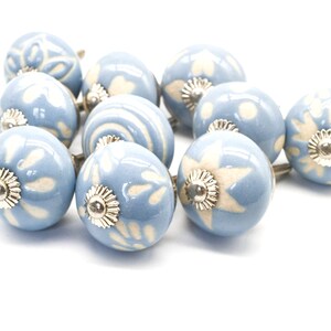 May include: A set of ten blue ceramic cabinet knobs with white floral designs. Each knob has a silver metal base.