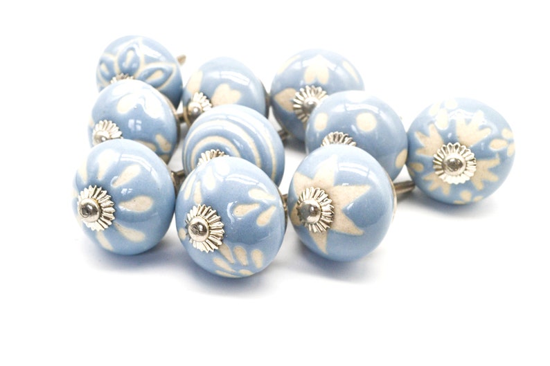May include: A set of ten blue ceramic cabinet knobs with white floral designs. Each knob has a silver metal base.