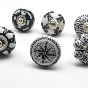 K&ouml;nnte beinhalten: Sechs schwarze und wei&szlig;e Keramik-Schubladengriffe mit verschiedenen Designs. Die Griffe haben einen goldenen Akzent in der Mitte.