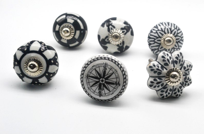 K&ouml;nnte beinhalten: Sechs schwarze und wei&szlig;e Keramik-Schubladengriffe mit verschiedenen Designs. Die Griffe haben einen goldenen Akzent in der Mitte.