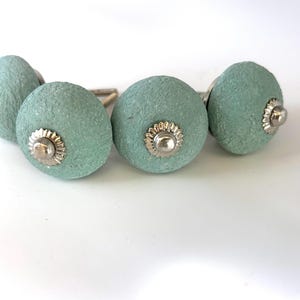 Puede incluir: Cuatro pomos redondos de armario verde mar con una superficie texturizada. Cada pomo tiene una base de metal plateado y un centro decorativo plateado. Estos pomos son ideales para a&ntilde;adir un toque de color y estilo a cualquier armario o caj&oacute;n.