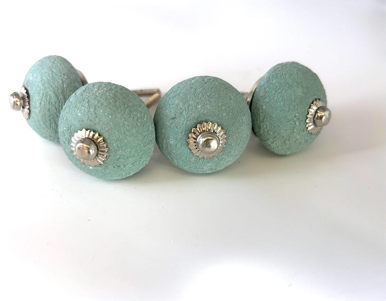 Puede incluir: Cuatro pomos redondos de armario verde mar con una superficie texturizada. Cada pomo tiene una base de metal plateado y un centro decorativo plateado. Estos pomos son ideales para a&ntilde;adir un toque de color y estilo a cualquier armario o caj&oacute;n.