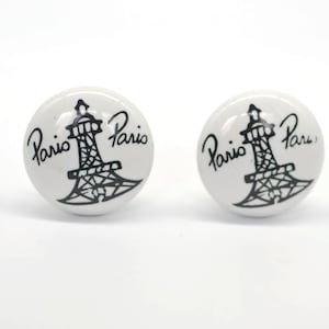 May include: Two white ceramic knobs with a black Eiffel Tower design and the text "Paris" on each knob.