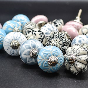 Może przedstawiać: Zestaw ceramicznych gałek do szuflad z różnymi wzorami kwiatowymi i geometrycznymi w odcieniach niebieskiego, białego, różowego, czarnego i zielonego. Gałki mają srebrne akcenty.