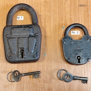 May include: Two antique metal padlocks with keys. One is a large, rectangular lock with the text "Nr. 1" and the other is smaller with the text "Nr. 2". Both locks are dark grey and show signs of age and wear.