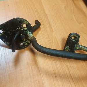 May include: A black metal door latch with a curved handle and a diamond-shaped plate. The latch has a worn, aged finish with some rust and green paint.
