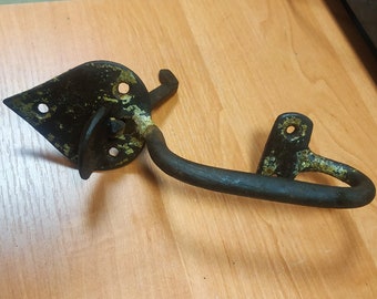 Puede incluir: Un pestillo de puerta de metal negro con una manija curva y una placa en forma de diamante. El pestillo tiene un acabado desgastado y envejecido con algo de óxido y pintura verde.