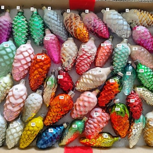 Könnte beinhalten: Eine Sammlung von 41 Vintage-Weihnachtsbaumschmuck aus Glas in Form von Tannenzapfen. Der Schmuck ist in verschiedenen Farben, darunter Grün, Rot, Pink, Weiß und Gold. Einige der Schmuckstücke haben eine matte Oberfläche.