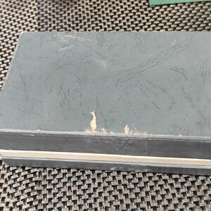 May include: A gray cardboard box with a white stripe around the edge. The box has a textured surface and appears to be slightly worn.