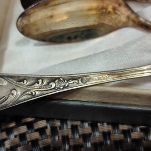 May include: Close-up of the back of a silver spoon with an ornate design and the inscription "Sterling 22/40".