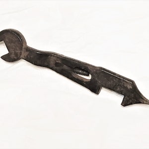 May include: A rusty, black metal wrench with a bottle opener on the end. The wrench has a small, round hole in the handle.