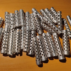 Peut inclure: Plusieurs bigoudis cylindriques en métal argenté, percés de nombreux petits trous. Ils sont disposés sur une surface en bois. Ces bigoudis sont conçus pour créer des boucles ou des ondulations dans les cheveux, un outil de coiffure classique.