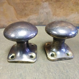 May include: Two antique brass door knobs with a rounded top and a square base. Each knob has four holes on the base.