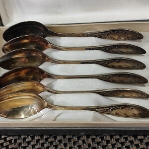May include: Set of six silver teaspoons with ornate handles in a velvet-lined box. The spoons are polished and have a vintage look.