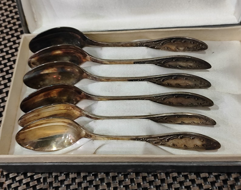 May include: Set of six silver teaspoons with ornate handles in a velvet-lined box. The spoons are polished and have a vintage look.