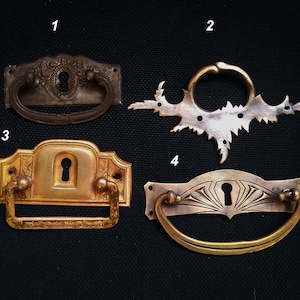 Może przedstawiać: Cztery antyczne uchwyty do szuflad z otworami na klucze. Uchwyty są wykonane z mosiądzu i mają różne wzory. Uchwyty są ponumerowane od 1 do 4.
