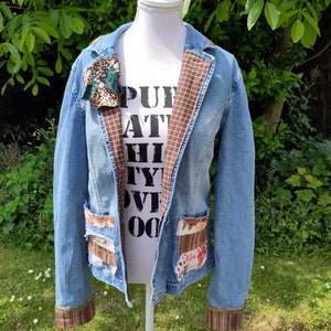 Könnte beinhalten: Eine blaue Jeansjacke mit braunem und weißem kariertem Stoff, der Kragen und Ärmel auskleidet. Die Jacke hat mehrere aufgenähte Patches auf der Vorderseite, darunter ein Leopardenmuster-Patch, ein Blumenpatch und ein braunes und weißes kariertes Patch. Die Jacke befindet sich auf einem weißen Mannequin.