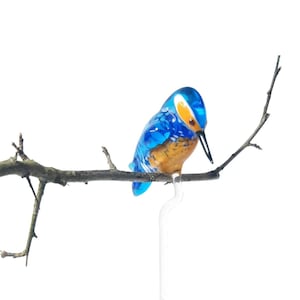 Könnte beinhalten: Eine blaue und orangefarbene Glasvogelfigur, die auf einem Ast sitzt. Der Vogel hat einen langen, dünnen Schnabel und detaillierte Markierungen.